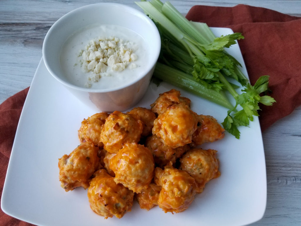 Buffalo Chicken Meatballs on a white plate with celery and blue cheese dressing
